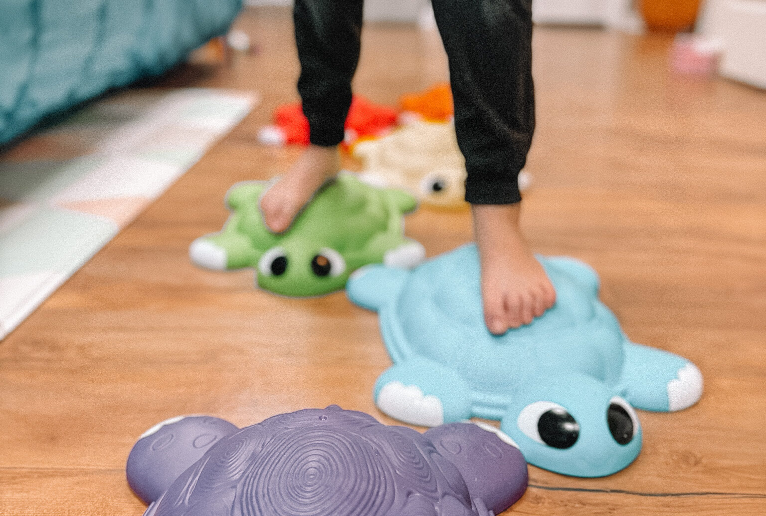 Black child's feet and lower legs walking across stuffed toys on the floor during a sensory play activity.